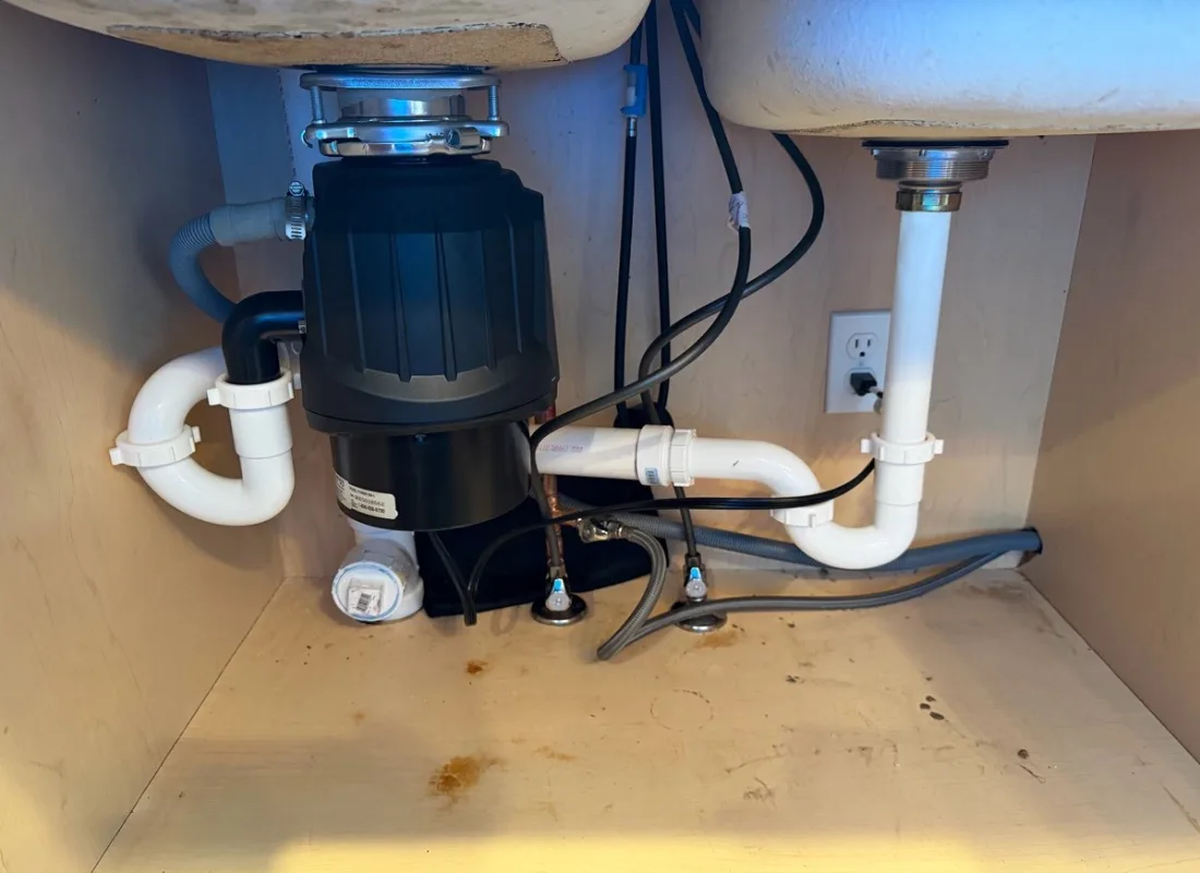 Newly fitted garbage disposal and trap under a kitchen sink