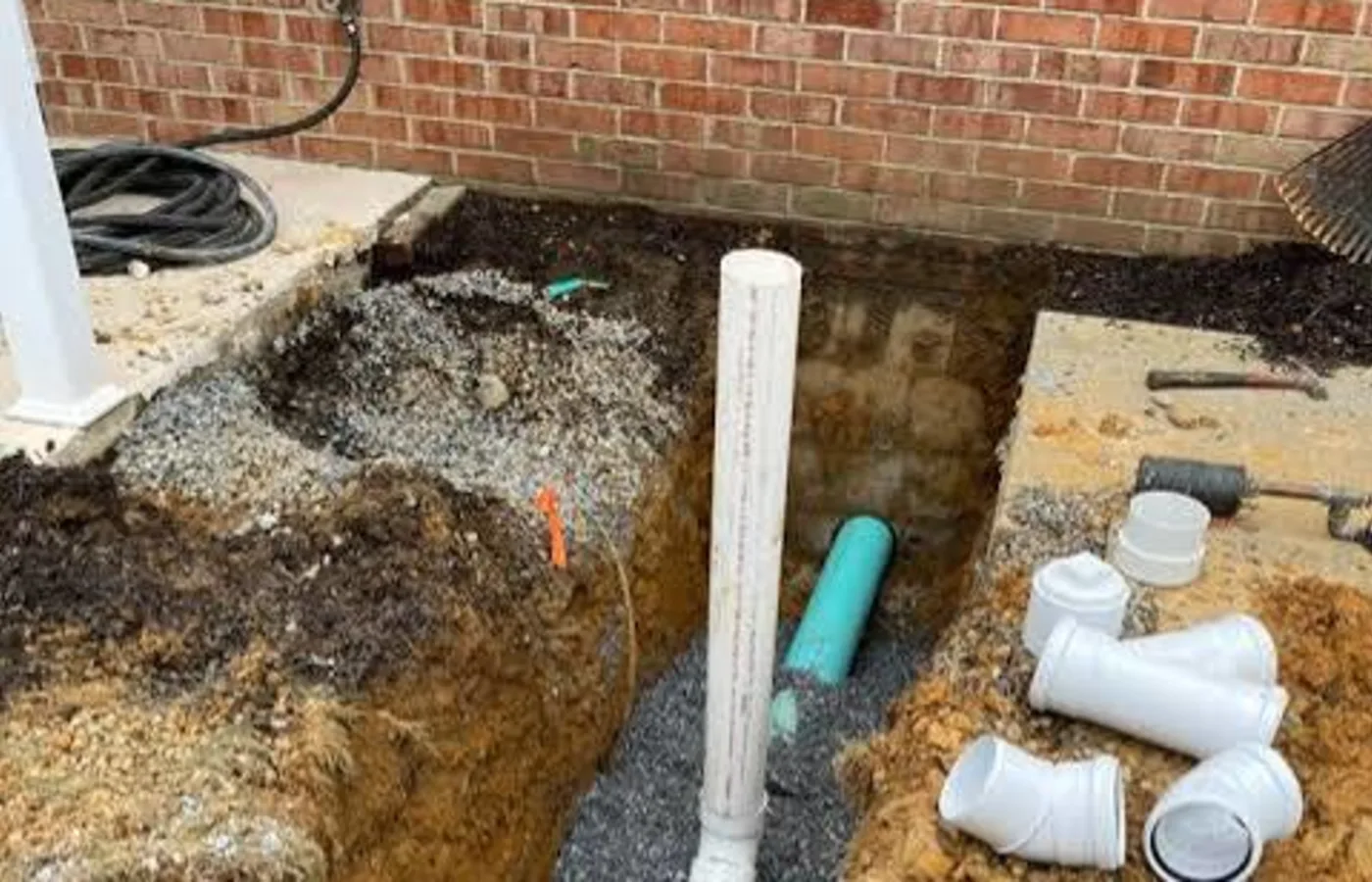 New sewer line and fittings set in an open trench beside a house
